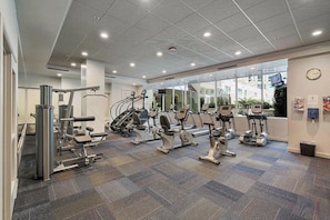 A gym with various cardio and strength equipment, large windows, and a patterned carpet. - Quiet North Waterfront 1BR · WFH Setup · in-unit W/D · 24/7 Doorman, Gym, Sauna (San Francisco)