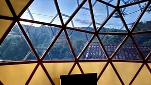 Ein Zimmer mit einem großen Fenster, das ein geometrisches Muster zeigt, einem Laptop auf einem kleinen Tisch und Blick auf eine gebirgige Landschaft.