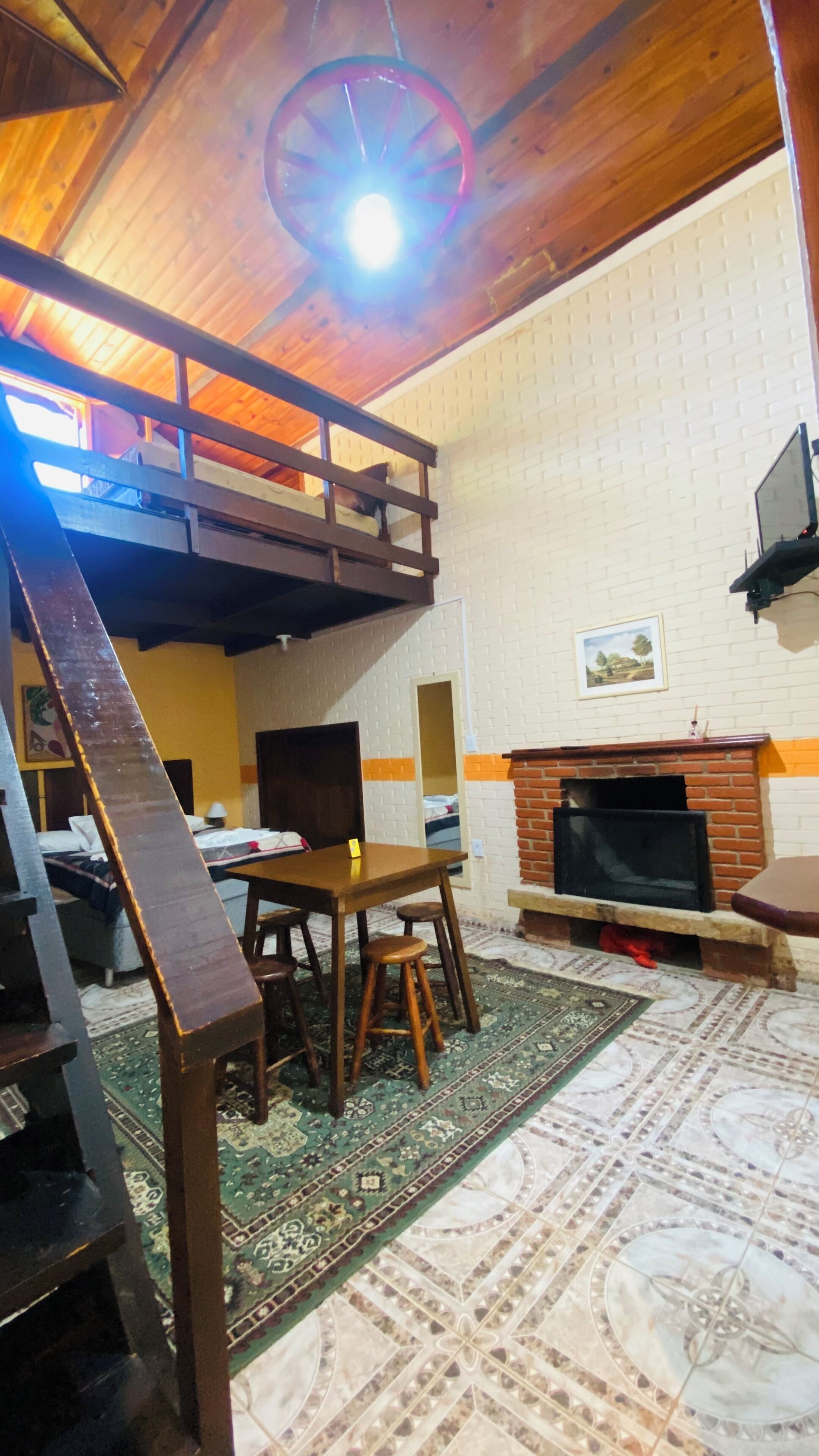 Une pièce avec un lit en mezzanine, une cheminée, une table à manger et un tapis à motifs.