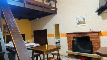Une pièce avec un lit en mezzanine, une cheminée, une table à manger et un tapis à motifs.