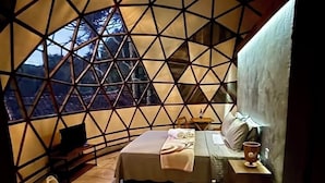 Ein Schlafzimmer mit Bett, Nachttisch und Blick durch ein fenster mit geometrischem Muster.