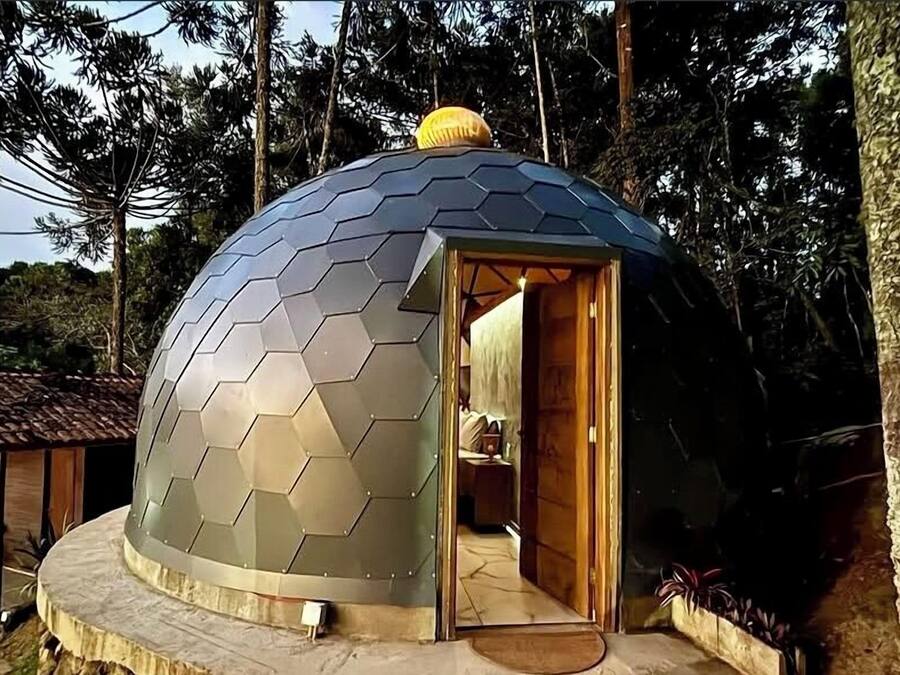 Una estructura de domo geodésico con un diseño hexagonal, una puerta de madera y un pequeño porche.