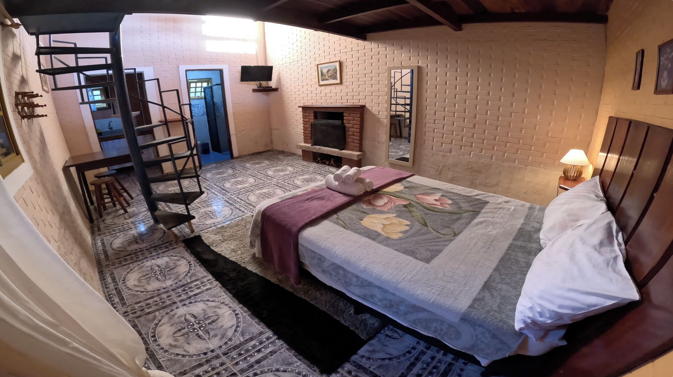 Um quarto com cama, lareira, televisão e escada.