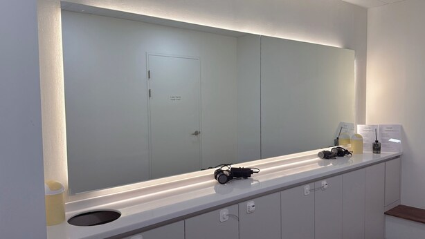 A modern bathroom with a large mirror, a white sink, and a door with a sign. - STAYUP ILSAN Capsule Hotel (Goyang)