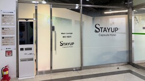 A Stayup Capsule Hotel entrance with a glass door, a vending machine, and a fire extinguisher. - STAYUP ILSAN Capsule Hotel (Goyang)