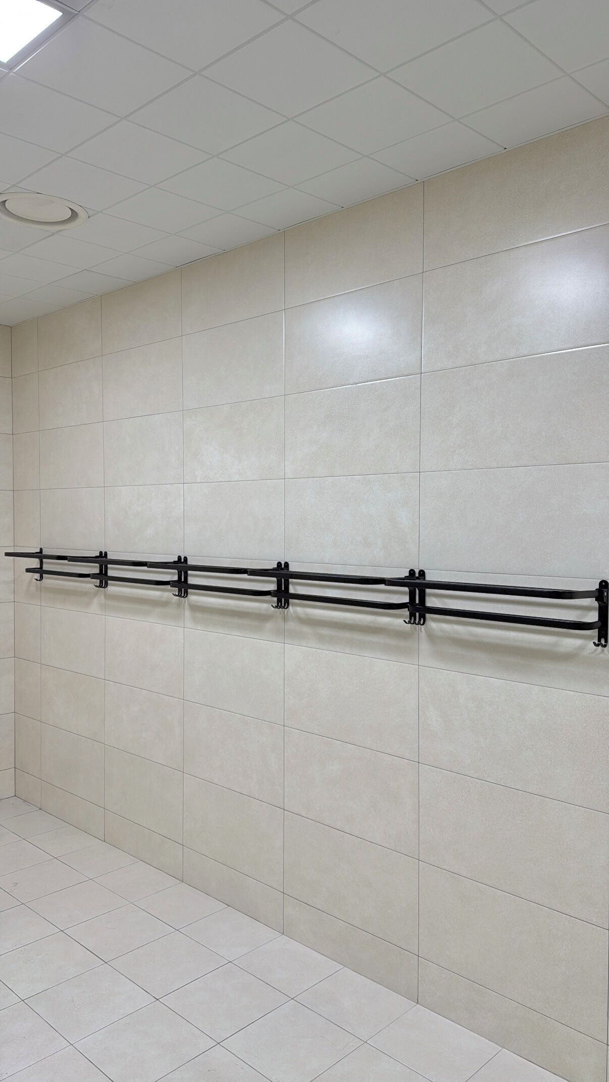 Una pared con azulejos y un estante metálico negro horizontal.
