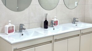 A bathroom with two sinks, three mirrors, and a tiled wall. - STAYUP ILSAN Capsule Hotel (Goyang)