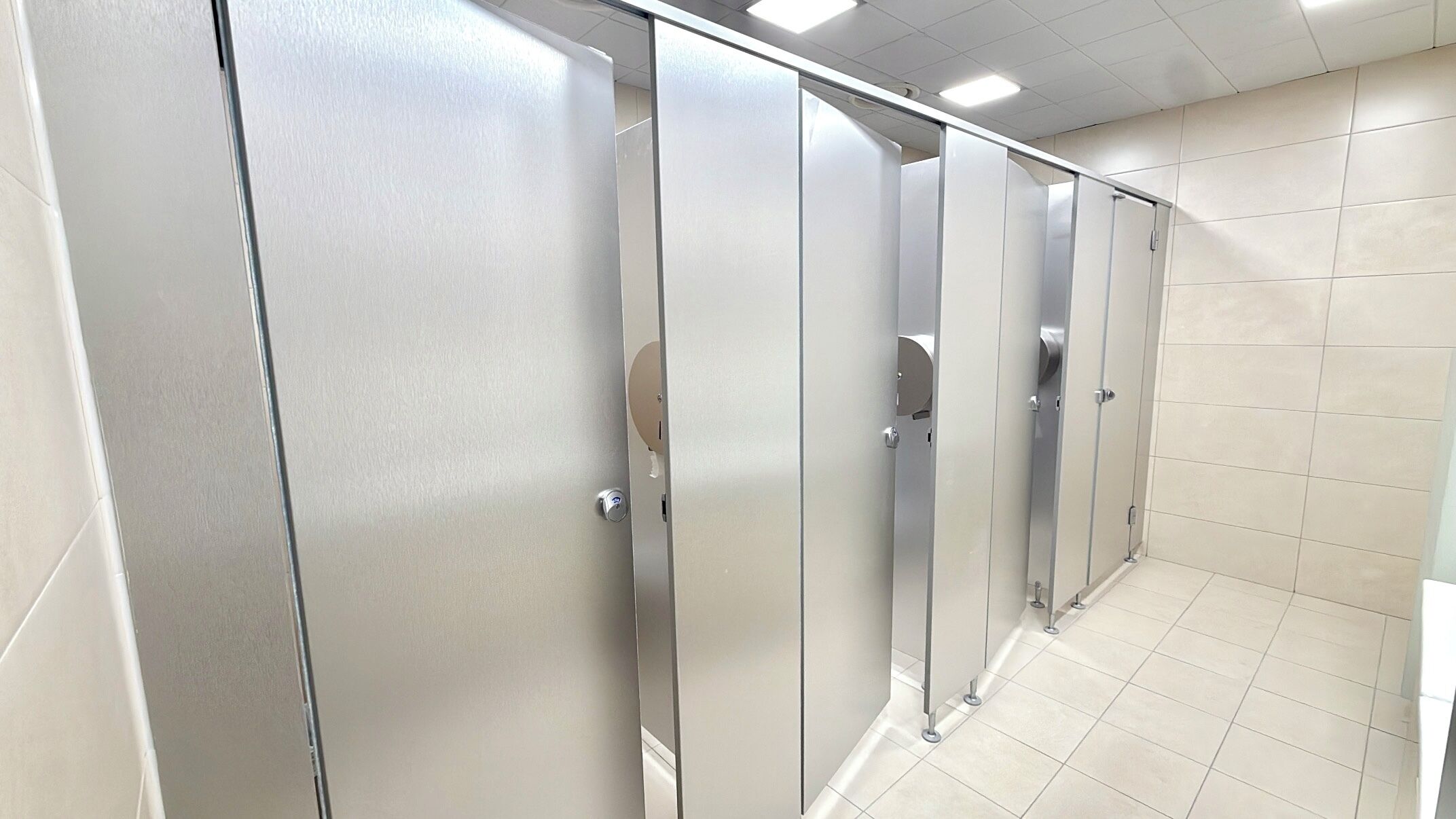 Une rangée de cabines de toilettes métalliques avec un sol carrelé.