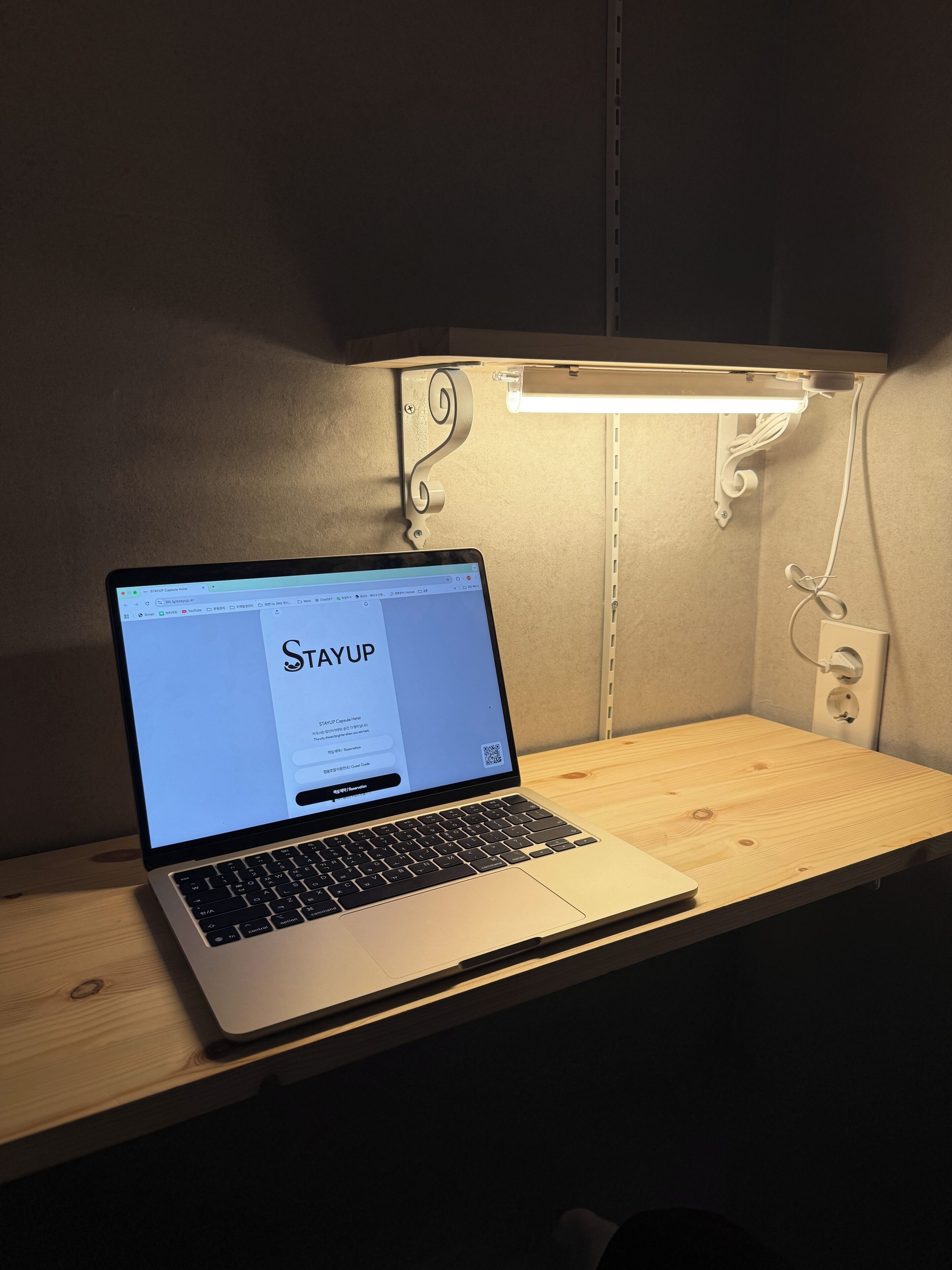 Una computadora portátil sobre un escritorio de madera con una lámpara fijada a la pared.