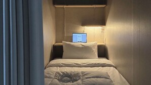 A small, dimly lit room with a single bed, a nightstand, and a wall-mounted computer screen. - STAYUP ILSAN Capsule Hotel (Goyang)