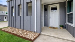 A modern two-story building with a grey exterior, a white door, and a small porch area. - 4BR Austin Home, Minutes to Downtown, Parking, Sleeps 10 (Austin)