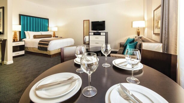 A hotel room with a bed, a TV, a dining table set with plates and wine glasses, and a sofa. - Convenient Acessible Studio Condo for Comic Con 2026 San Diego (San Diego)