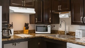 A kitchen with dark wooden cabinets, a white refrigerator, a coffee maker, a microwave, a toaster, and a sink. - Convenient Acessible Studio Condo for Comic Con 2026 San Diego (San Diego)