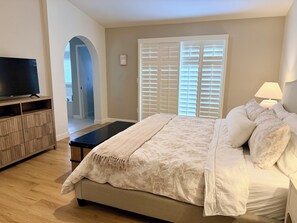Un dormitorio con una cama, un televisor sobre un soporte, una lámpara y una puerta con persianas.