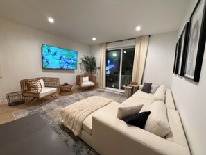 A modern living room with a sofa, two armchairs, a TV, and a large window with a view. - Bohemian Getaway at the Jersey Shore (Seaside Heights)