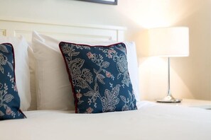 A neatly made bed with white bedding and decorative pillows with floral patterns. - Milsoms Hotel (Kenilworth)