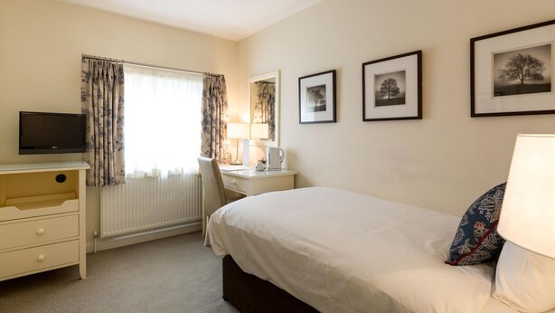 A hotel room with a bed, a desk with a TV, a chair, a lamp, and framed pictures on the wall. - Milsoms Hotel (Kenilworth)