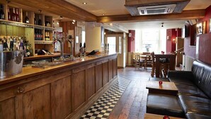A bar area with wooden shelves, a checkered floor, a leather couch, and a dining area with chairs and a table. - Milsoms Hotel (Kenilworth)