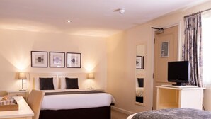 Une chambre d’hôtel avec un lit, des tables de chevet, un bureau, une télévision et des tableaux encadrés accrochés au mur.