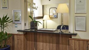 A reception desk with a potted plant, framed certificates, and a lamp. - Milsoms Hotel (Kenilworth)
