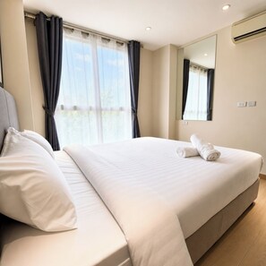 A hotel room with a large bed, a window with curtains, a mirror, and an air conditioning unit. - Tropical Resort Escape | Grande Caribbean Pattaya (Bang Lamung)
