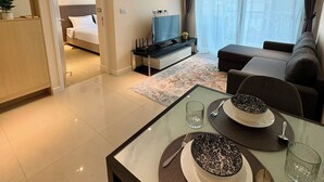 Ett modernt hotellrum med en säng, en soffa, en TV och en matplats med ett bord dukat för två personer.