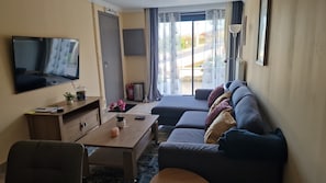 Ein Hotelzimmer mit einer Couch, einem Fernseher, einem Schreibtisch und einem Fenster mit Vorhängen.