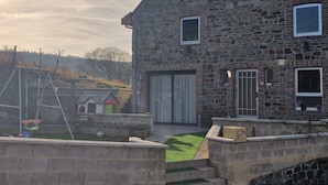 A stone building with a large garage door, a small garden with artificial grass, and a swing set. - The Famenne Escape (Marche-en-Famenne)