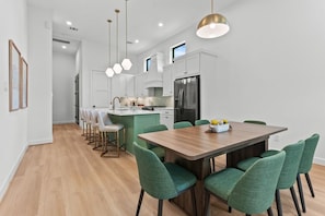 A modern kitchen with white cabinets, a central island, and a dining area with green chairs. - Luxury 7BR/7BA Home • Houston Skyline • Downtown (Houston)