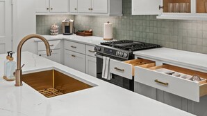 Una cocina moderna con armarios blancos, un lavamanos de acero inoxidable, una estufa a gas y una cafetera.