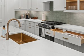 A modern kitchen with white cabinetry, a stainless steel sink, a gas stove, and a coffee maker. - Luxury 7BR/7BA Home • Houston Skyline • Downtown (Houston)