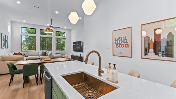 Una cocina moderna con una isla central, un comedor con sillas verdes, un sofá y un televisor.