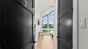 Un pasillo moderno con puertas negras, suelo de madera, un escritorio y una cama con vistas al cielo.