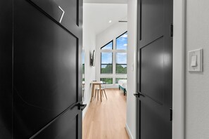 A modern hallway with black doors, a wooden floor, a desk, and a bed with a view of the sky. - Luxury 7BR/7BA Home • Houston Skyline • Downtown (Houston)