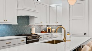 Eine moderne Küche mit weißen Schränken, einem Edelstahlherd, einem goldfarbenen Wasserhahn und einer Marmorarbeitsplatte.