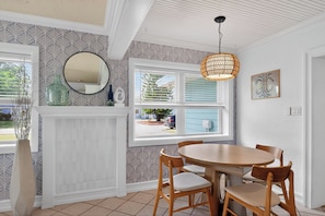 A dining area with a round wooden table and chairs, a hanging light fixture, a mirror, and a window with blinds.