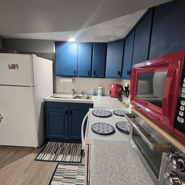 A kitchen with blue cabinets, a white stove, a red microwave, and a white refrigerator.
