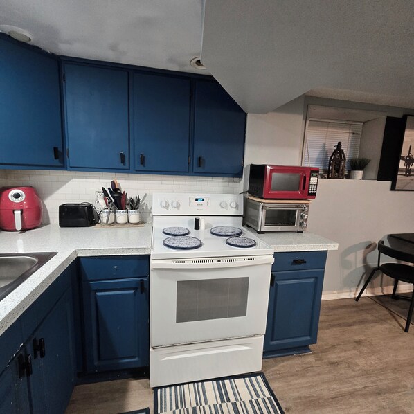Una cocina con armarios azules, una estufa blanca, un microondas rojo y un tostador.