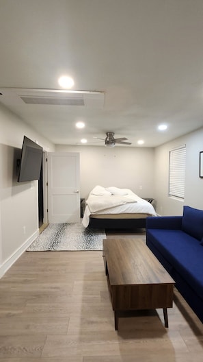 A bedroom with a bed, a ceiling fan, a TV mounted on the wall, a wooden bench, and a blue sofa. - Beautiful 2-bedroom house with AC in welcoming Glendale (Glendale)