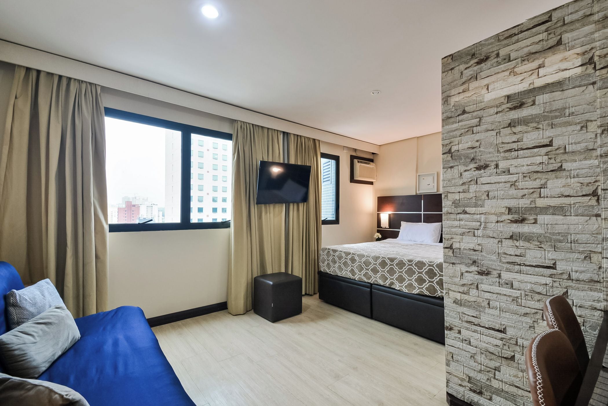 A hotel room with a bed, a TV, a desk, and a view of the city.