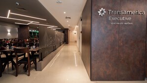 A modern interior with a long corridor, wooden tables, and chairs, and a wall with 'Transamerica Executive' signage. - RCT Hospedagens - Chácara Santo Antonio (São Paulo)
