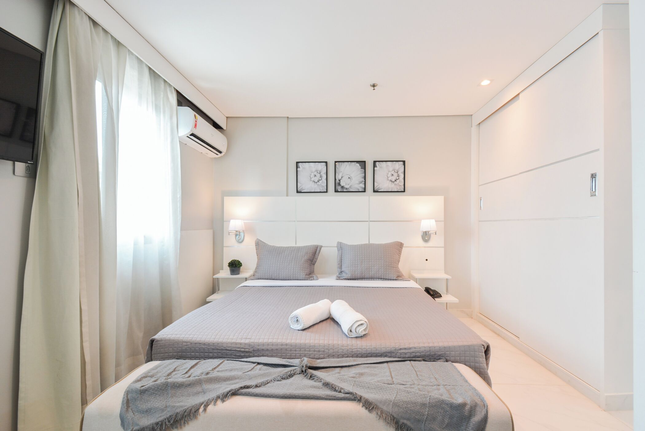 Habitaci ón de hotel con cama, mesita de noche, aire acondicionado y televisor montado en la pared.