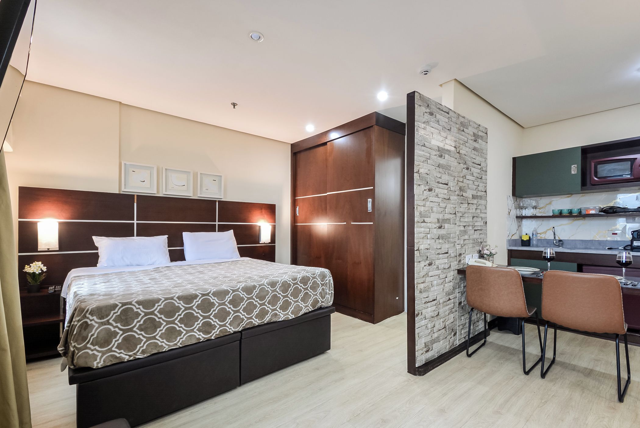 A hotel room with a bed, bedside table, and a kitchenette area.