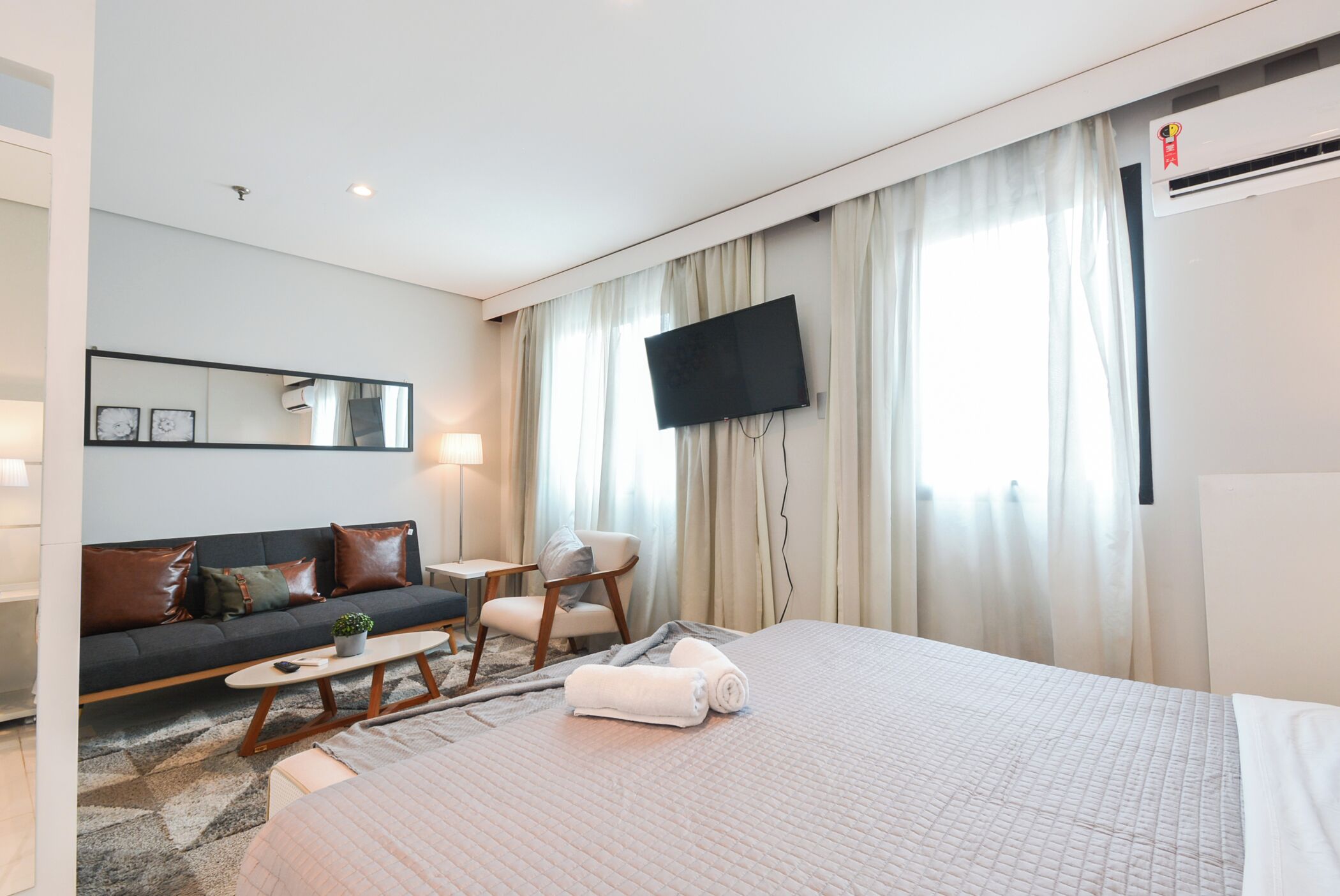 A hotel room with a bed, a sofa, a chair, a TV, and a window with curtains.