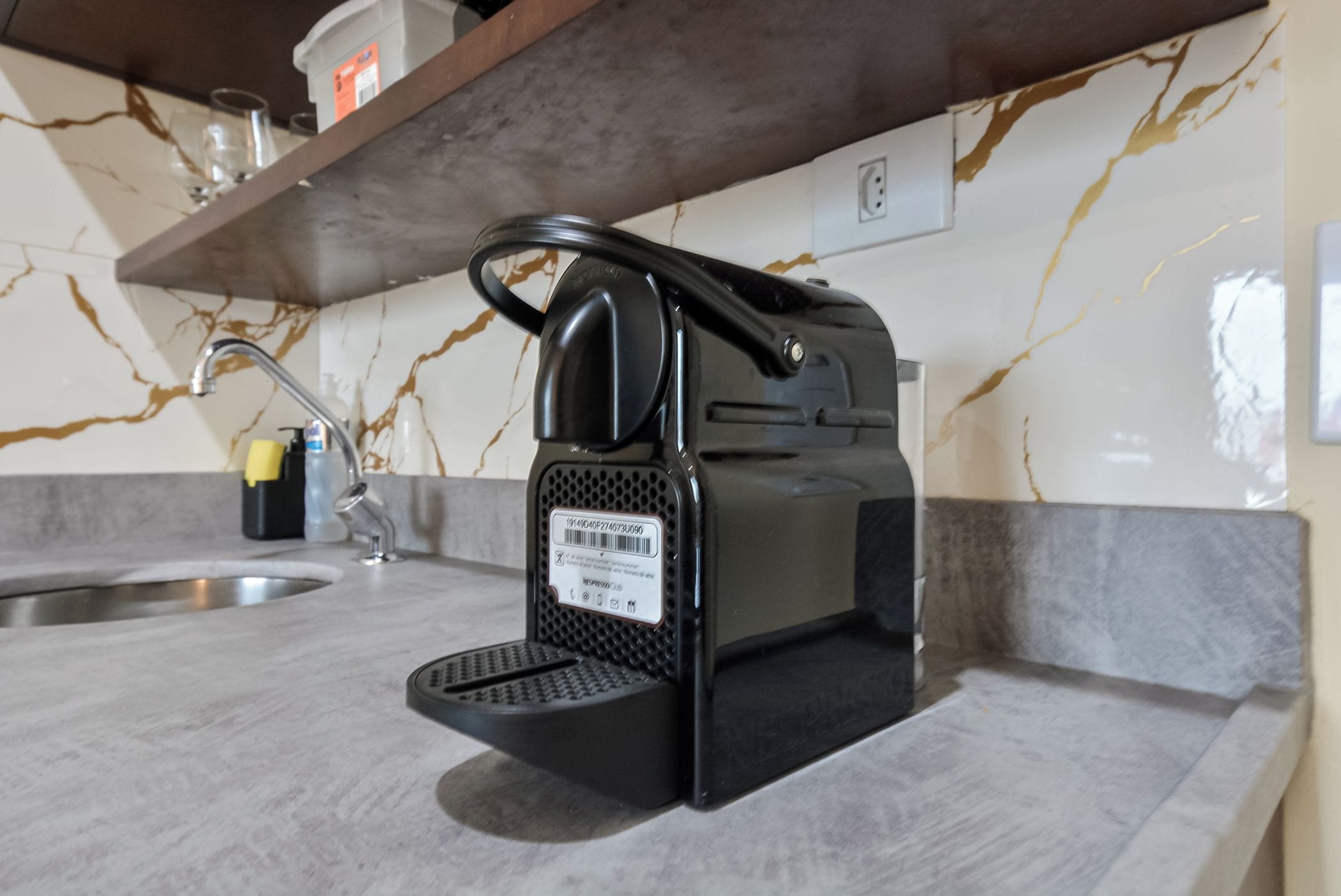 A kitchen with a coffee maker on the counter, a sink, and a marble backsplash.