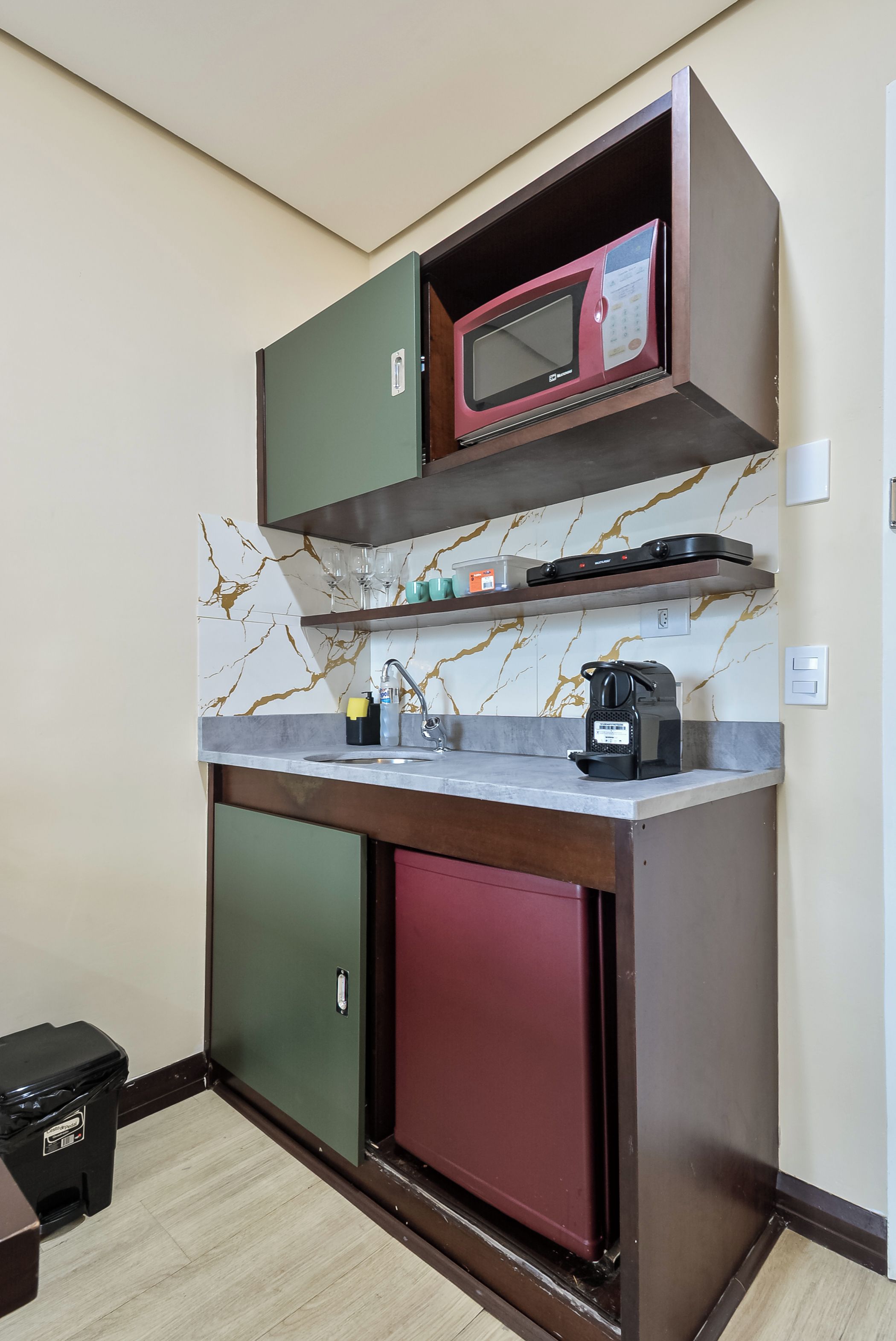 Een compacte kitchenette met een magnetron, een koffiezetapparaat en een kleine koelkast.