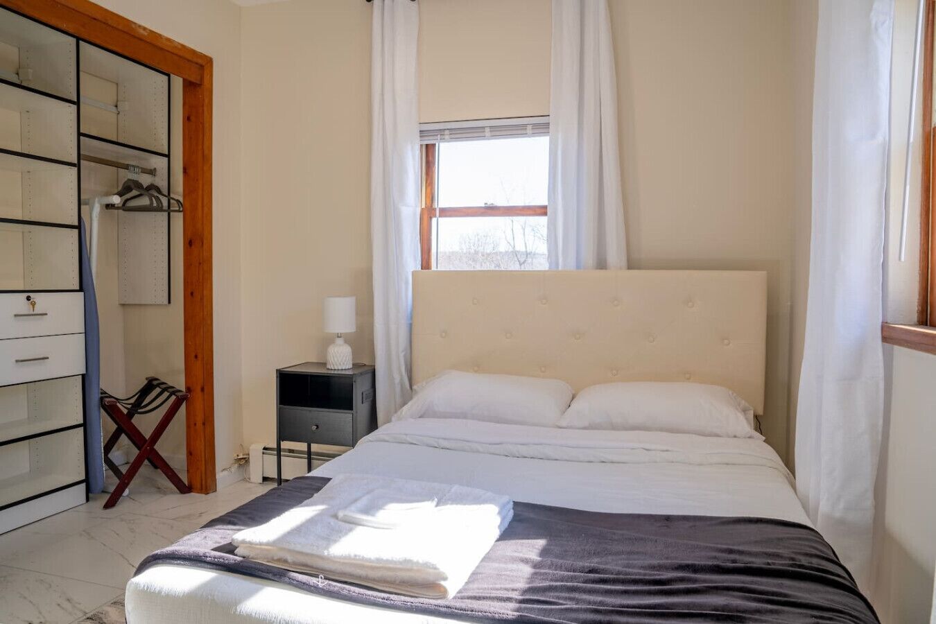 A bedroom with a bed, a nightstand, a wardrobe, and a window with curtains.