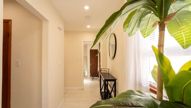 A hallway with a wooden door, a black table with a sign, and large green plants. - 3BR Near West Point | Coffee Bar | Sleeps 6 (Highland Falls)