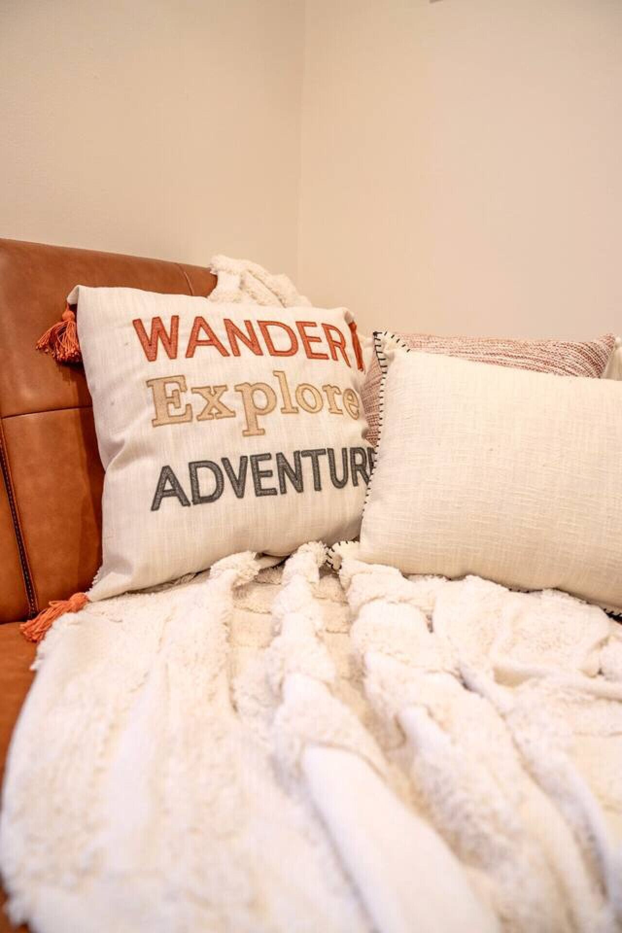 Una cama con una manta blanca y dos almohadas, una con el texto 'WANDER ADVENTURE'.