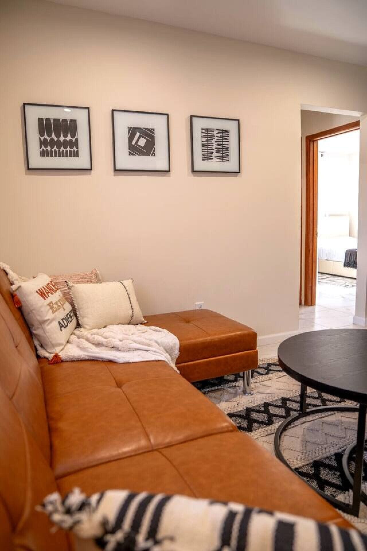 A living room with a brown sofa, a round table, and three framed artworks on the wall.